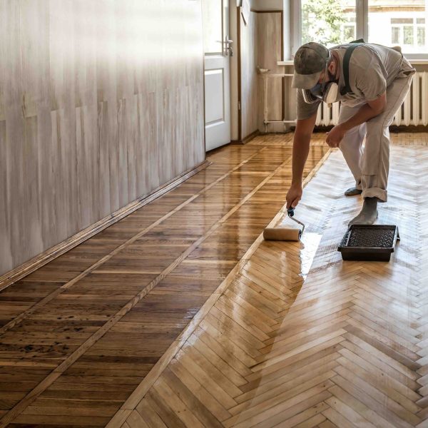 Flooring professional applying finish to a herringbone parquet hardwood floor in an older home.